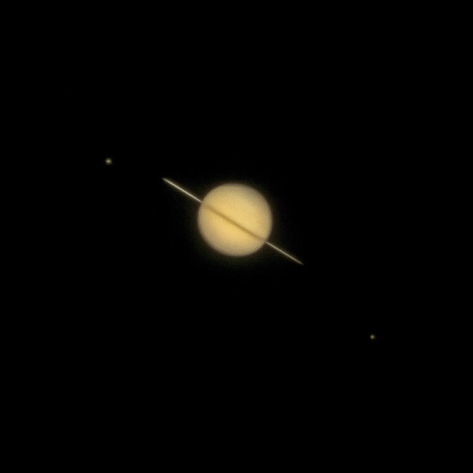 Saturn and its rings seen through a telescope, with two of its moons as small dots nearby