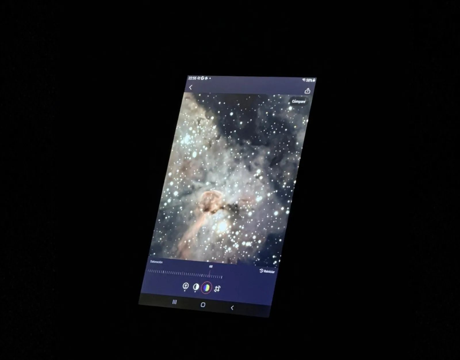 A tablet screen held in the dark shows a color image of a glowing nebula captured during the observation