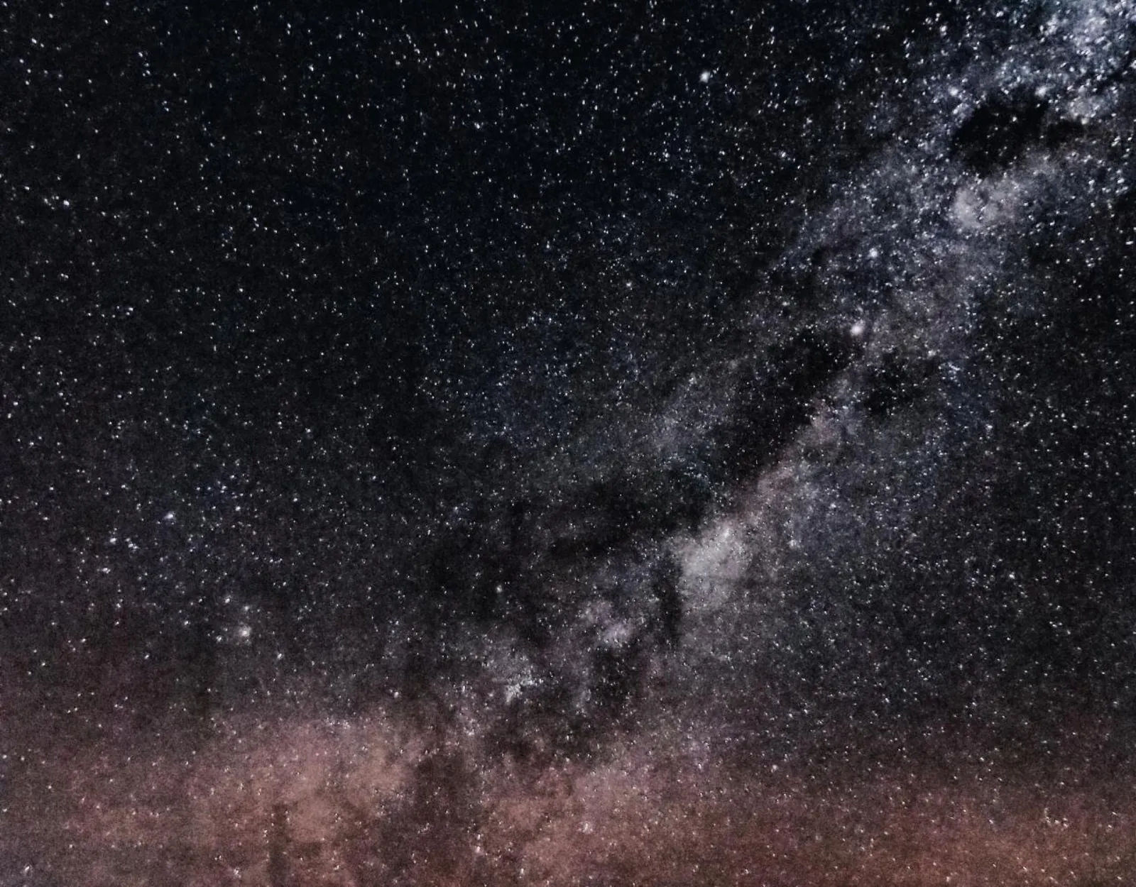 The Milky Way with dark dust lanes stretches diagonally across a dense star field above the Atacama Desert