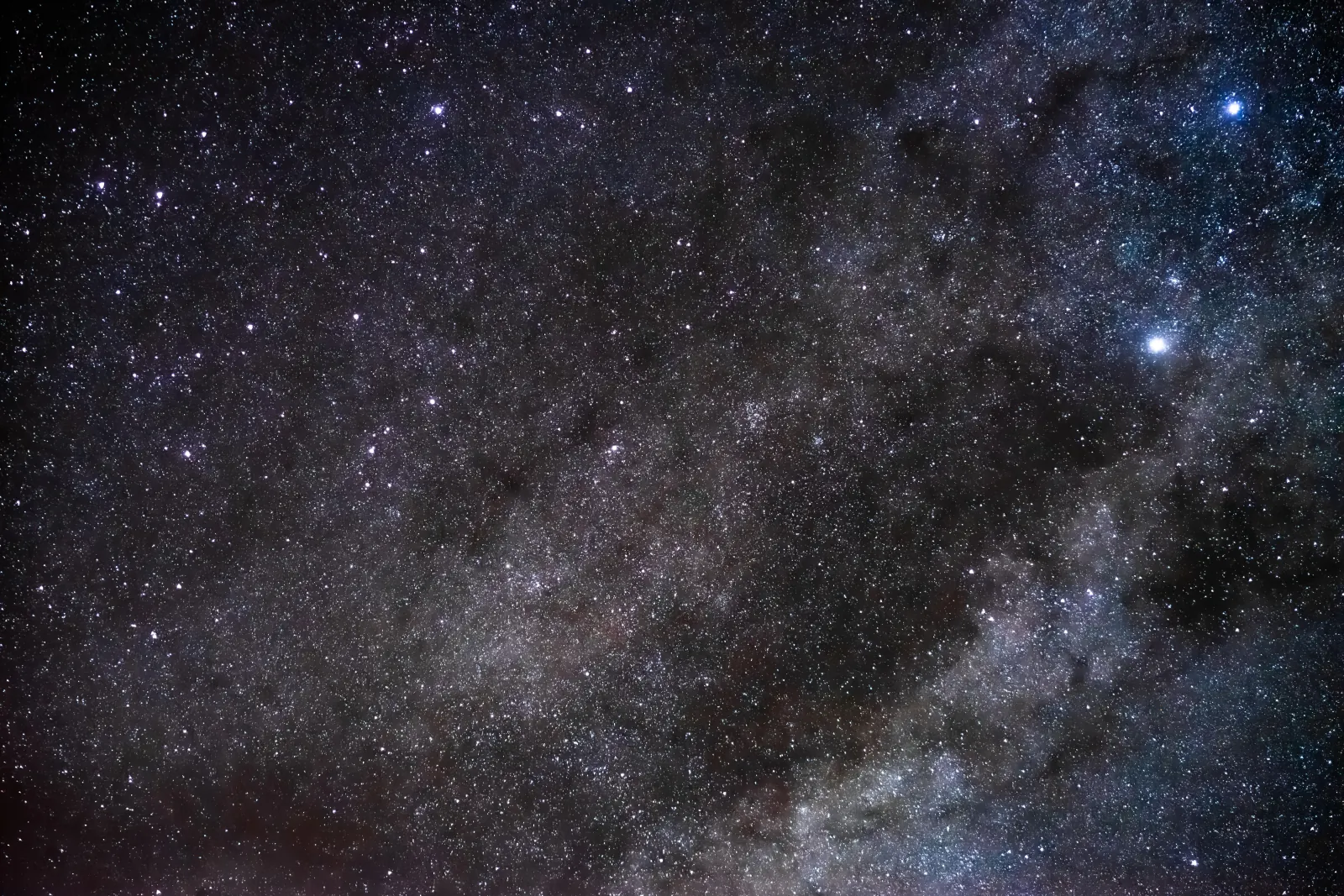 A dense star field and dark dust lanes of the Milky Way with bright stars, photographed from the Atacama