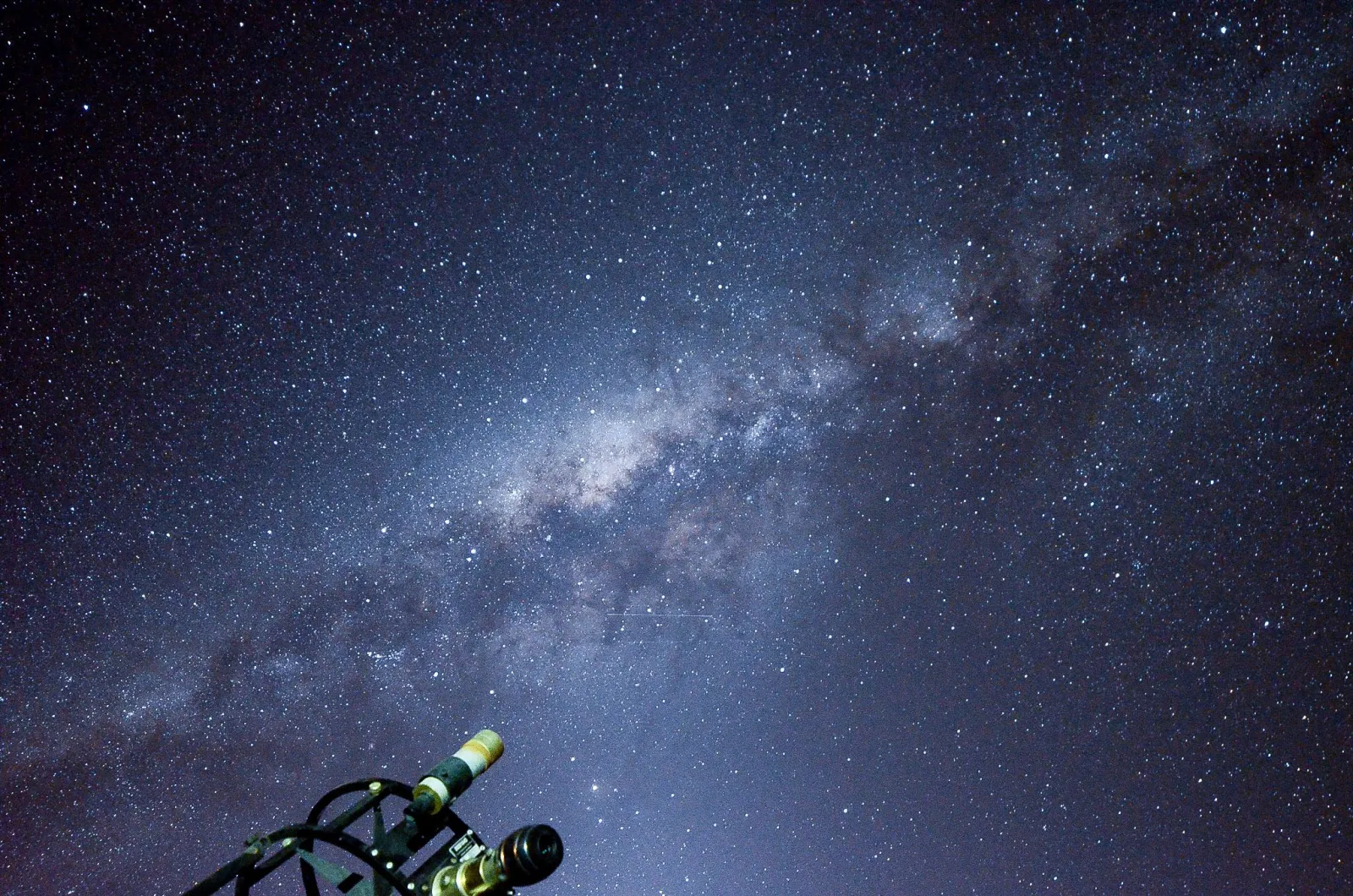 A refractor telescope on its mount points into a sky filled with stars and the bright core of the Milky Way