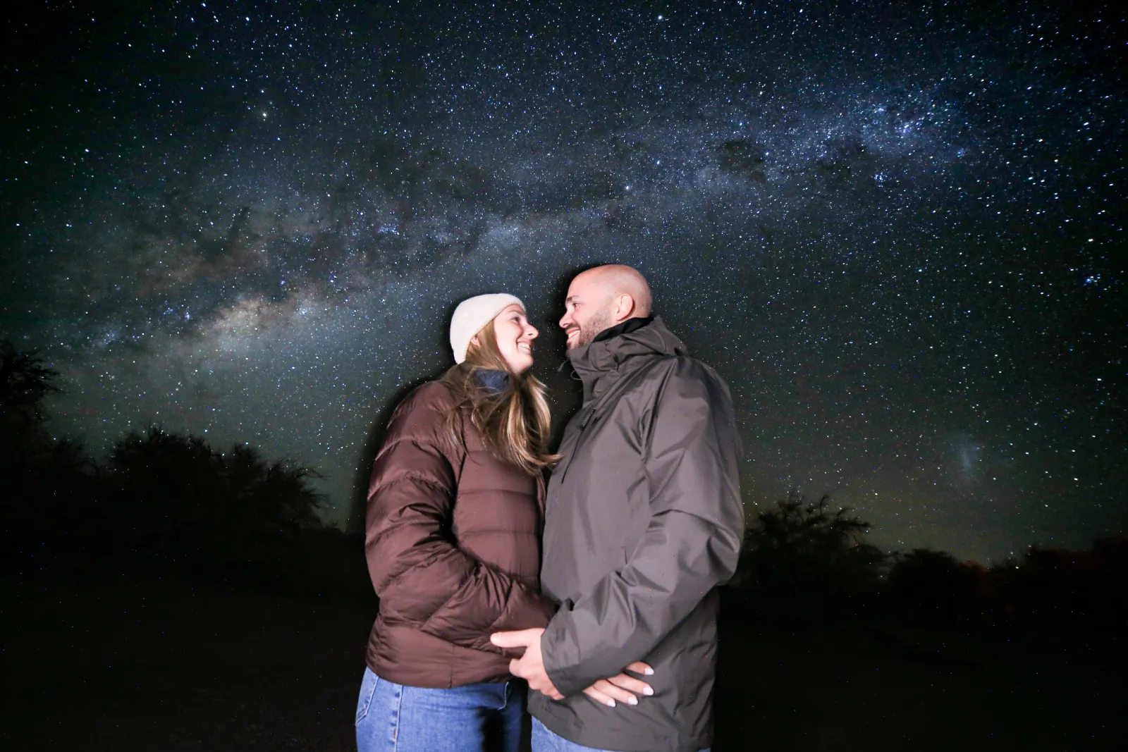 A couple in puffer jackets embraces under the Milky Way at a dark observation site outside San Pedro
