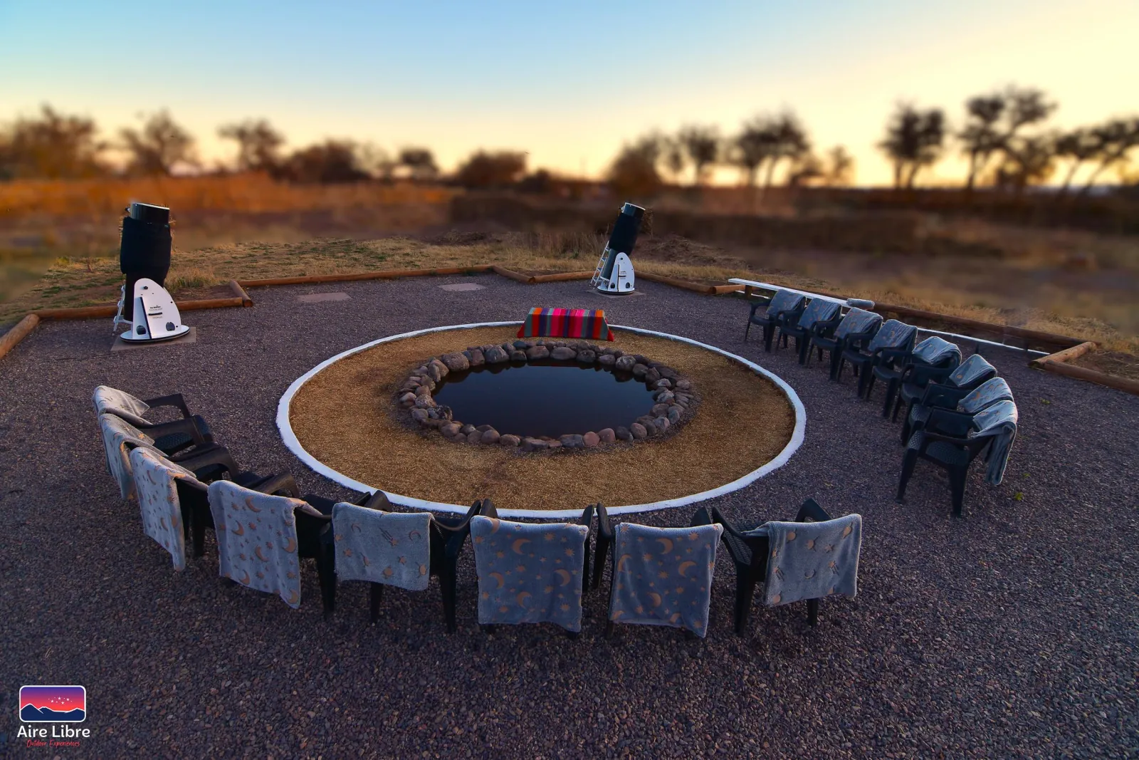 The aire libre site by day, with chairs and blankets ringing a stone-edged water pool and two telescopes nearby
